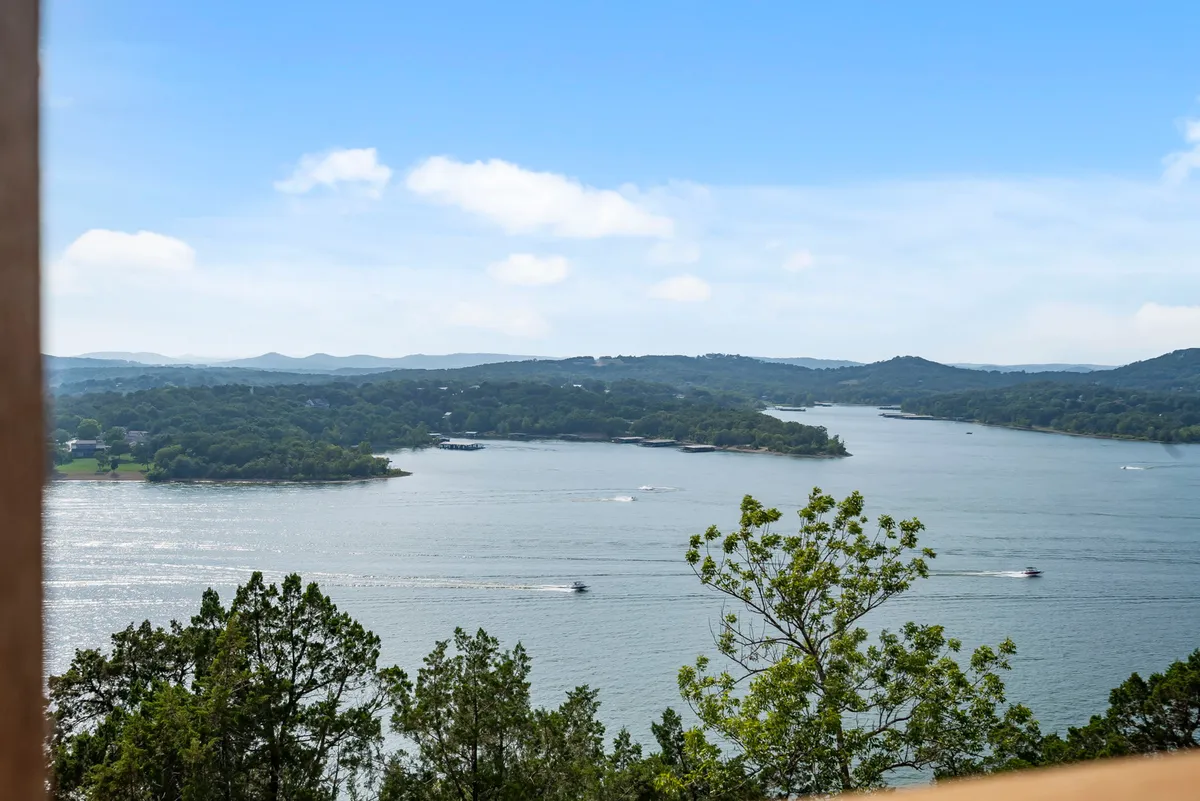 A tranquil lakeside view captures the expansive waters of Table Rock Lake with distant hills and visible boating activity. The scene is framed by lush tree lines, perfectly illustrating the lake’s recreational offerings and natural beauty.