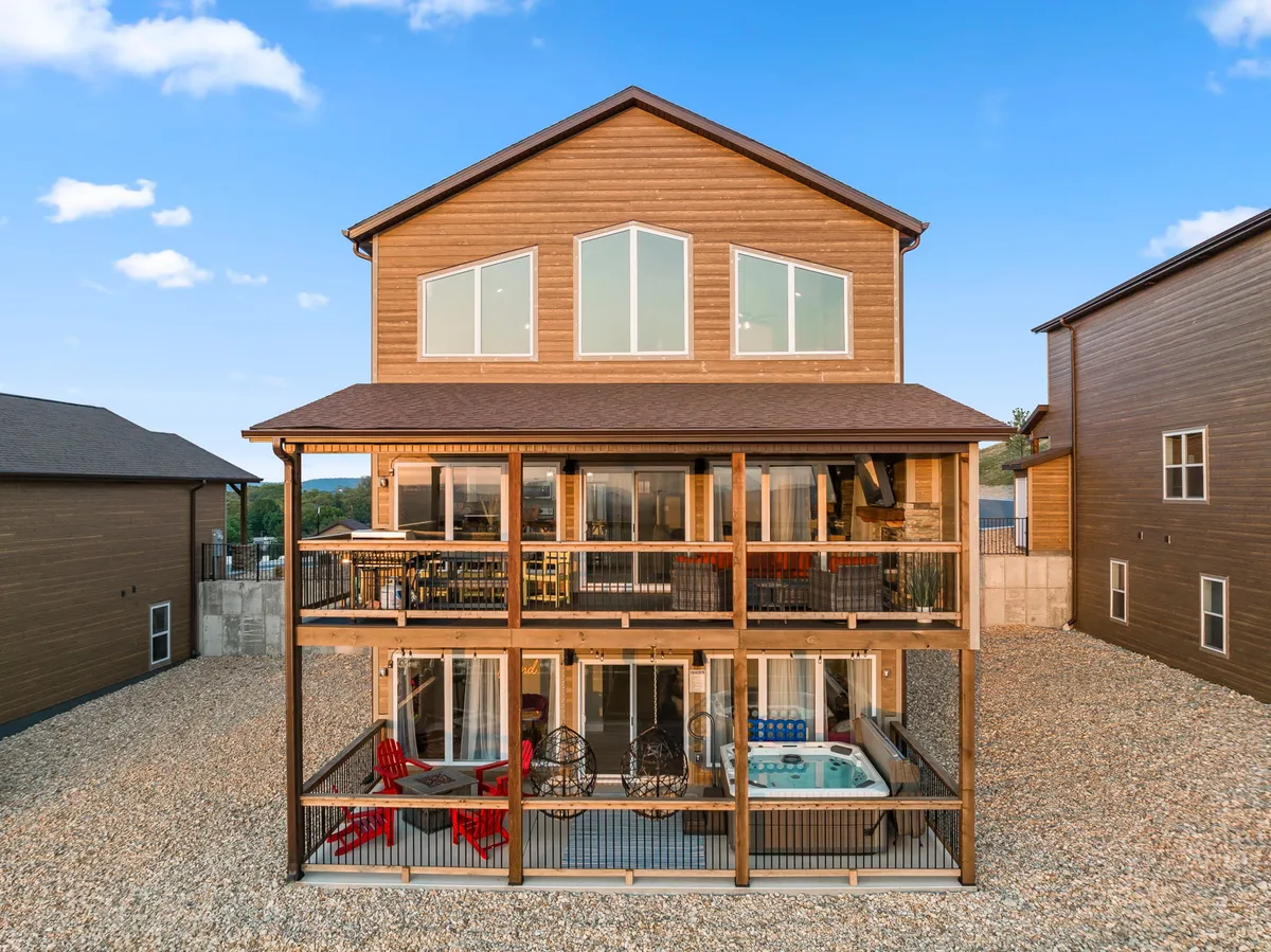 This exterior image showcases a multi-level deck overlooking the lake, featuring a hot tub, hanging chairs, and large windows. The deck invites relaxation with its ample seating and provides a direct connection to the scenic outdoors, ideal for both sunbathing and stargazing.