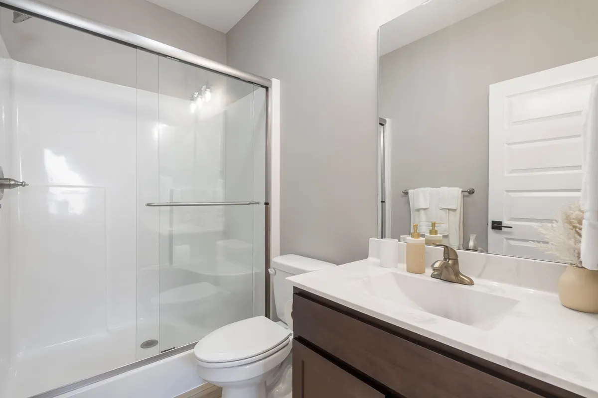 A modern ensuite bathroom featuring a glass shower enclosure, vanity with sink, and stylish decorative elements. The space looks clean, bright, and inviting, exemplifying convenience and privacy.