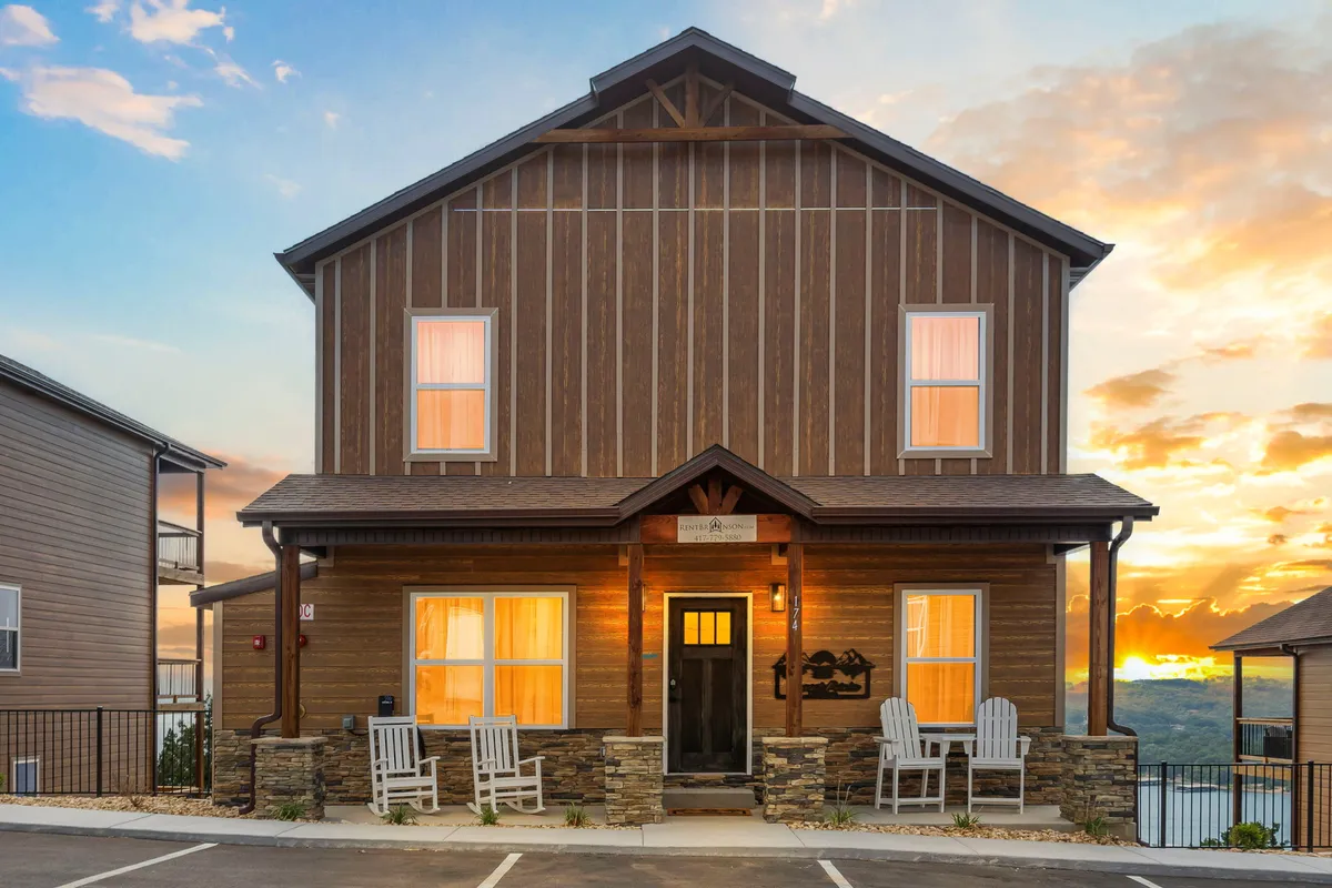 A view of the home's wooden exterior with rock accents, a front porch with seating, and a beautiful sunset backdrop. The image frames the property as warm and approachable, highlighting modern construction and outdoor relaxation space.