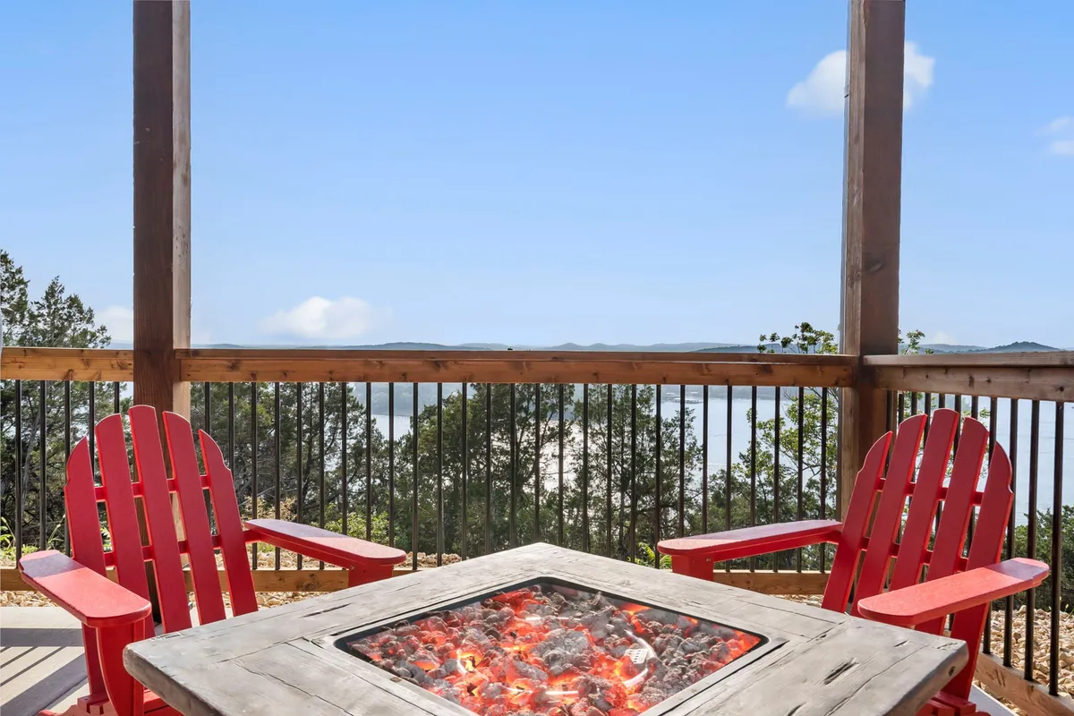 A cozy fire pit area with red Adirondack chairs overlooks a sweeping landscape, inviting guests to gather, socialize, and enjoy the tranquil evening views. The scene embodies lakeside camaraderie and relaxation.