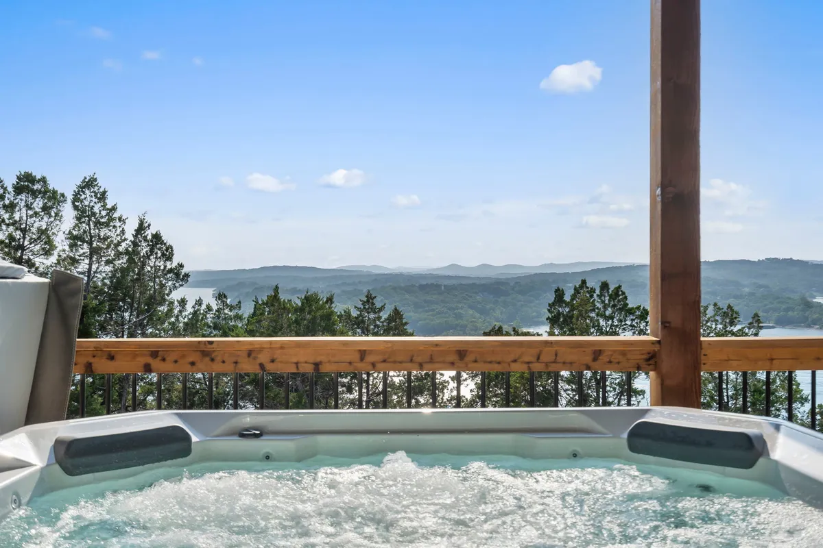 An inviting hot tub sits on a deck overlooking the lake and surrounding landscape. The wooden railing and open view create a relaxing atmosphere perfect for sunset soaks or stargazing.