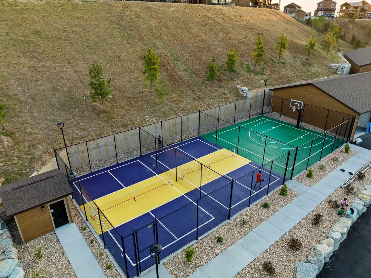 A bright, open view of multi-sport courts nestled in a lush landscape, featuring a basketball area and plenty of space for tennis or other group games. The courts are designed for friendly matches and community events, offering both recreation and opportunities for connection.