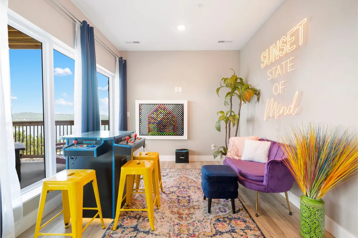 A lively game room filled with arcade machines, a glowing neon sign, vibrant and colorful furniture including a plush couch, and lush potted plants. The scene radiates energy, with inviting spaces for playing games and relaxing with friends.